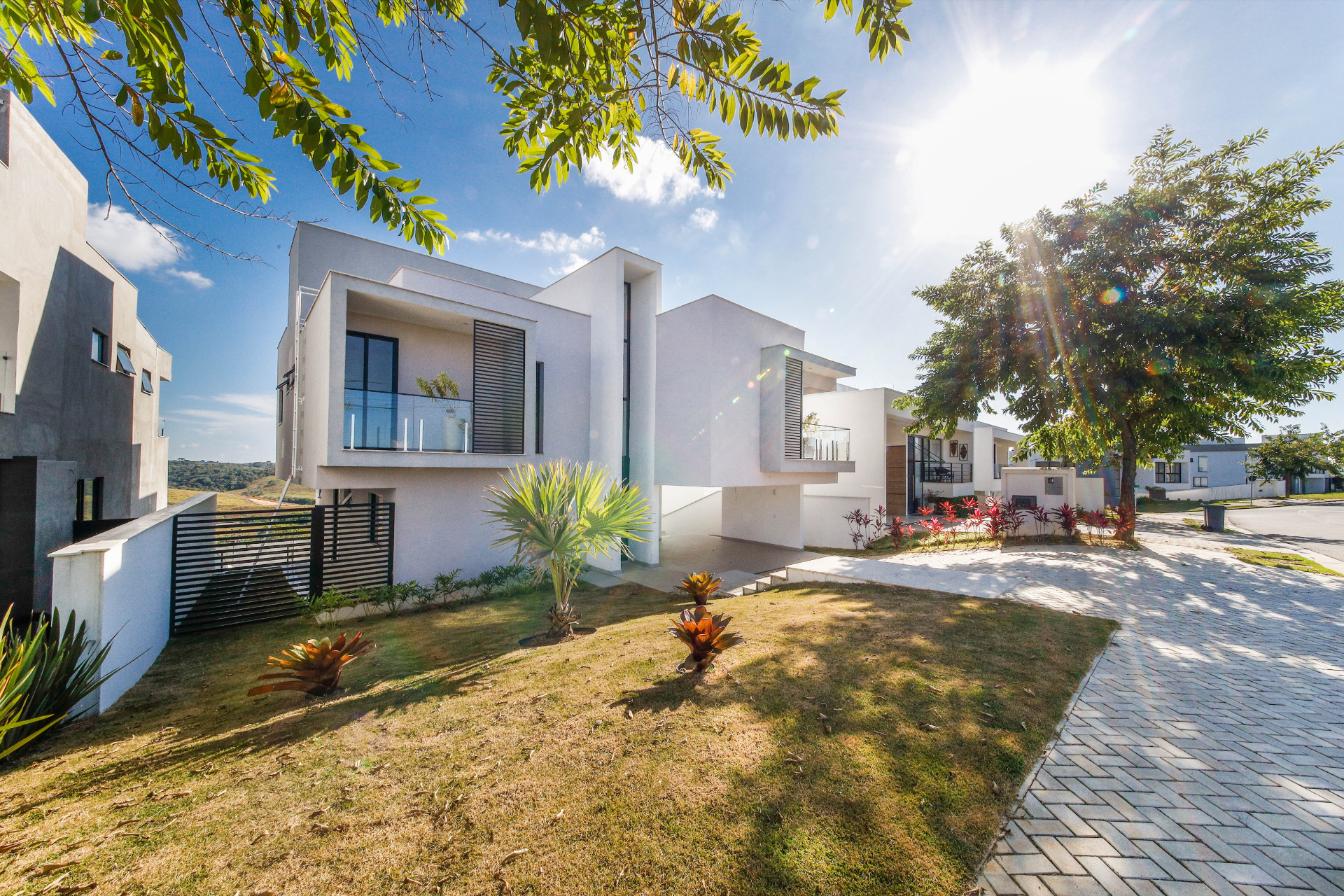 Residência de dois pavimentos com volumes brancos, varanda em vidro e jardim frontal