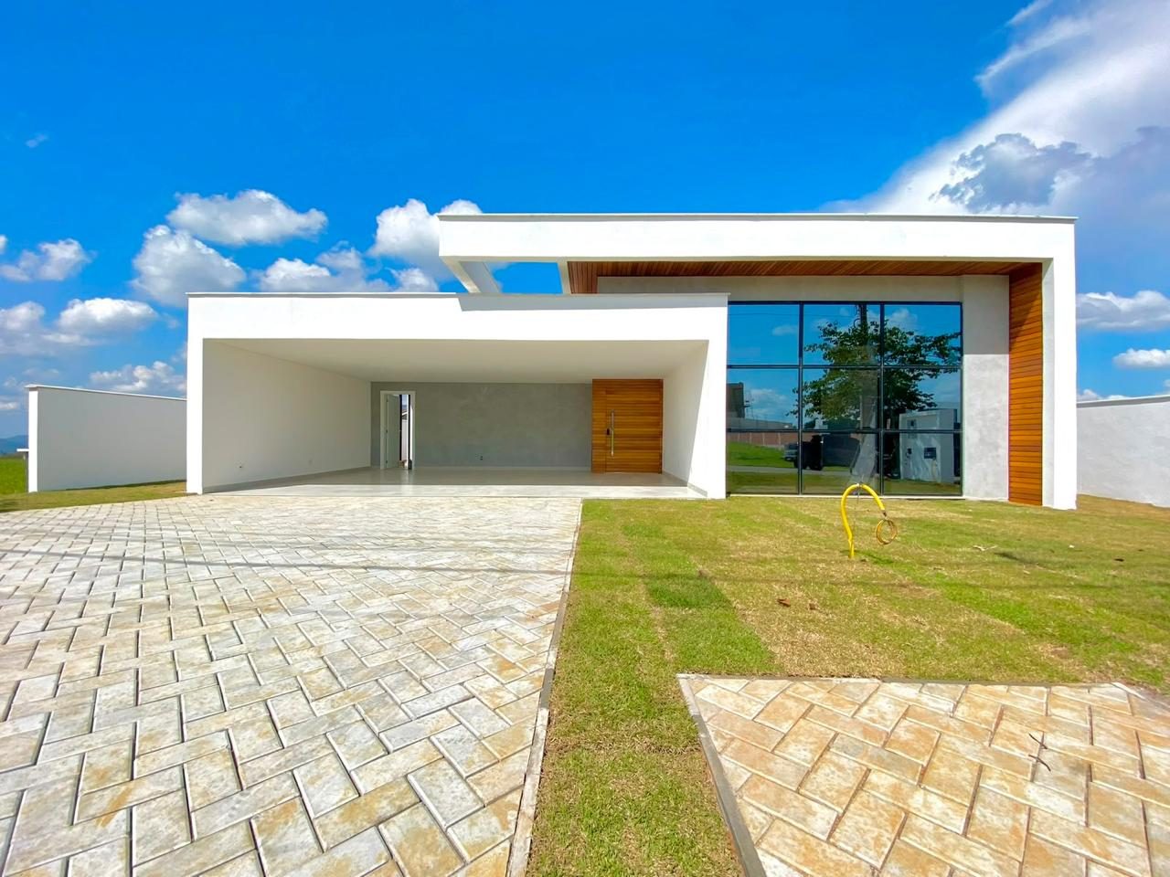 Residência térrea com fachada branca, porta pivotante em madeira e garagem coberta